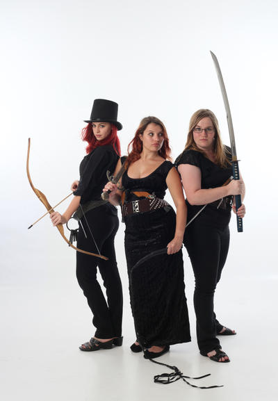 three women in dark fantasy costumes stand against a white background, each armed with a different weapon. one holds a bow and arrow, another a katana, and the third a shorter sword. they are dressed in black clothing, with varying hairstyles and accessories, including one woman wearing a top hat. the image has a dark and powerful aesthetic.
