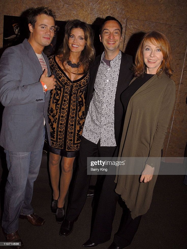 four friends pose for a photo together at a formal event. they are all dressed up in stylish attire, including a suit, dress, and sweater. they are smiling and appear to be having a good time. the photo is taken indoors, possibly at a gala or party. the lighting is dim, adding to the ambiance of the event.