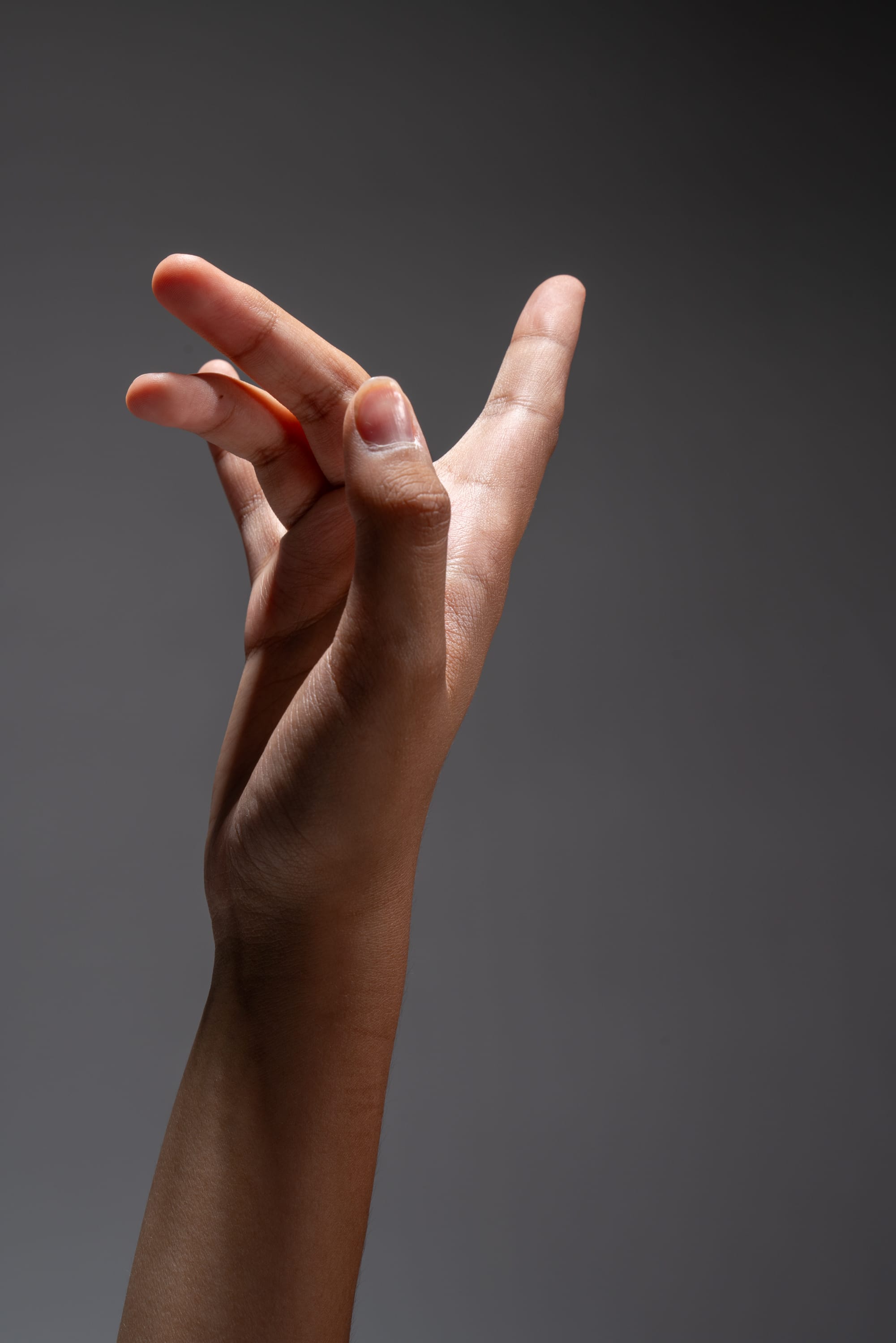 a closeup image of a hand against a grey background. the hand is posed with fingers slightly curled, showcasing the texture and detail of the skin. the lighting is dramatic, with a bright light highlighting the hand against the dark background.