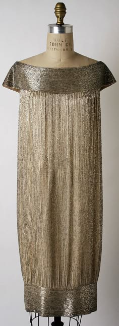 a vintage 1920s flapper dress made of golden fabric with a beaded and sequined trim. the dress is on a mannequin and the image is taken from the front.