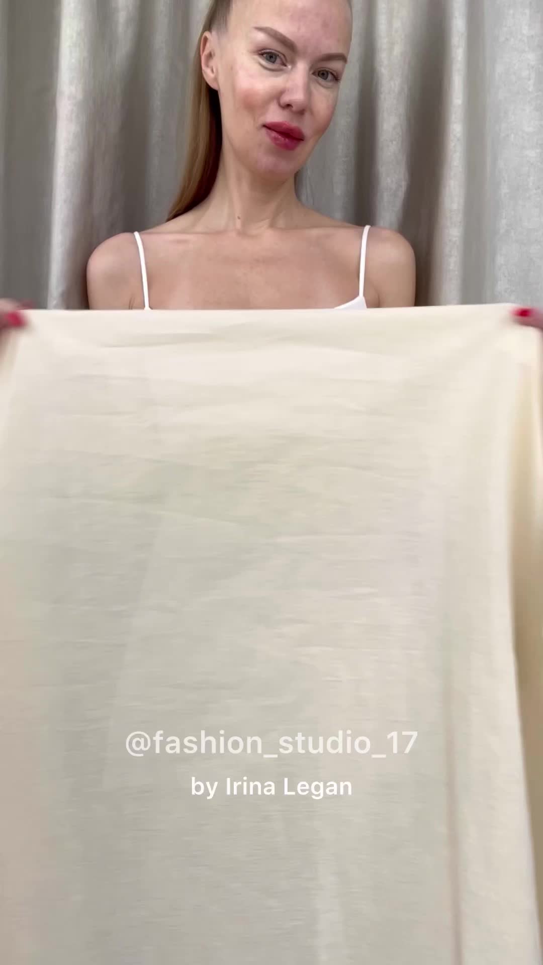 a woman with blonde hair wearing a white tank top is holding up a piece of light beige fabric in front of her. she is in a studio with a curtain behind her. the text "@fashion_studio_17 by irina legan" is visible on the fabric.