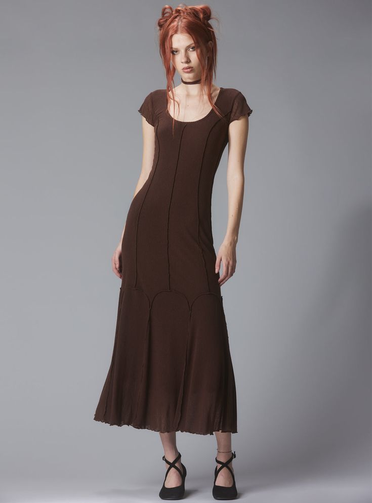 a full shot of a woman with vibrant red hair styled in two buns, wearing a dark brown maxi dress. the dress features short sleeves, a scoop neckline, a fitted bodice, and a flared skirt with subtle detailing along the hemline. she's wearing black anklestrap shoes and a simple choker necklace. the background is a neutral gray. the overall style is elegant and somewhat retro. the model stands in a poised pose, presenting the dress effectively.