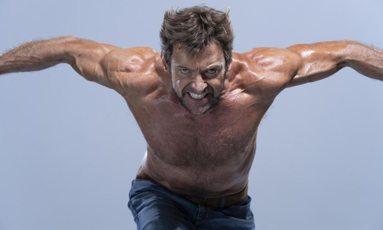 a shirtless hugh jackman as wolverine with muscular arms outstretched, looking angry with clenched teeth. he is wearing jeans. the image is a studio portrait with a plain background.