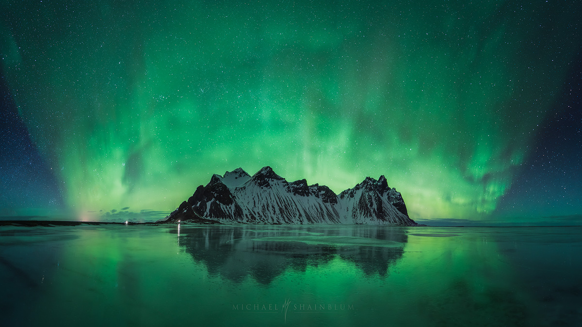 a breathtaking landscape shot of the aurora borealis reflecting on a still lake in front of snowcapped mountains. the aurora borealis, also known as the northern lights, is a natural light display in the sky, predominantly seen in the highlatitude regions (around the arctic and antarctic). the vibrant green hues of the aurora borealis paint the sky with an ethereal glow, creating a surreal and magical scene.