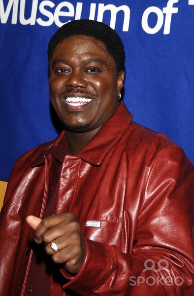 a portrait of a happy smiling black man wearing a red leather jacket against a blue background. the man is posing and giving a thumbs up.