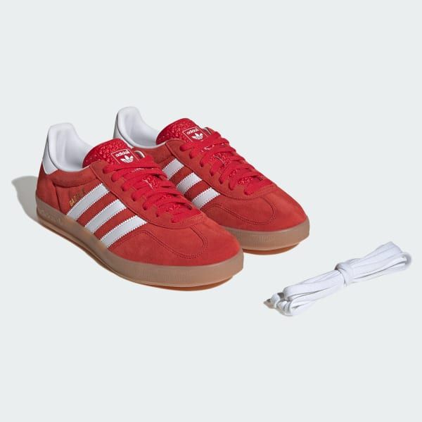 a pair of red adidas sneakers with white laces and stripes on the side.  the sneakers have a gum sole and are laying on a white background.  there is a white lace sitting next to them.