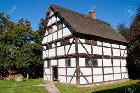 a photo of an old, wellpreserved white timberframed house with a thatched roof. the house is two stories tall and has many small windows. the house is surrounded by a grassy lawn and there are trees in the background. the sky is blue and sunny.