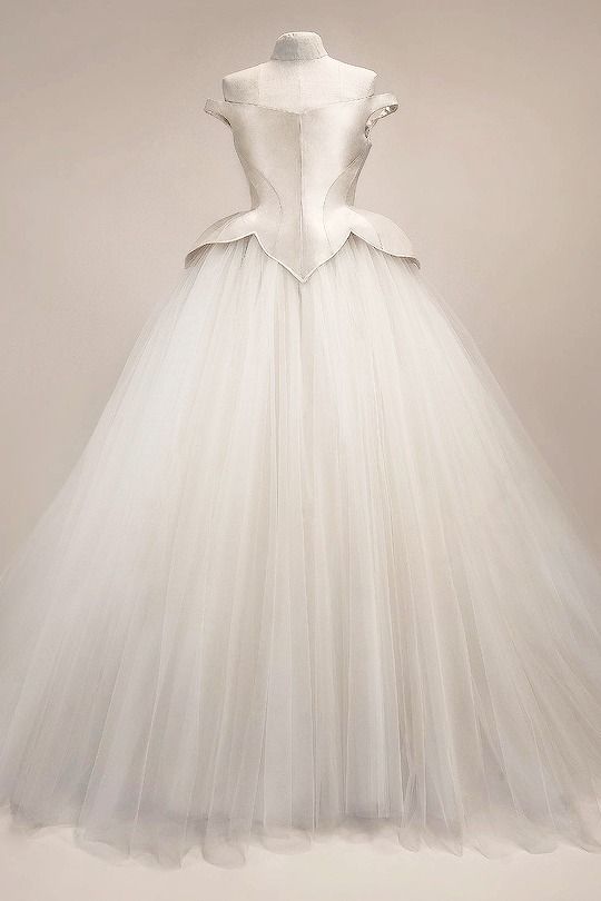 a white, offtheshoulder wedding dress is displayed on a mannequin. the dress is a ball gown style with a fitted bodice and a full, flowing tulle skirt.