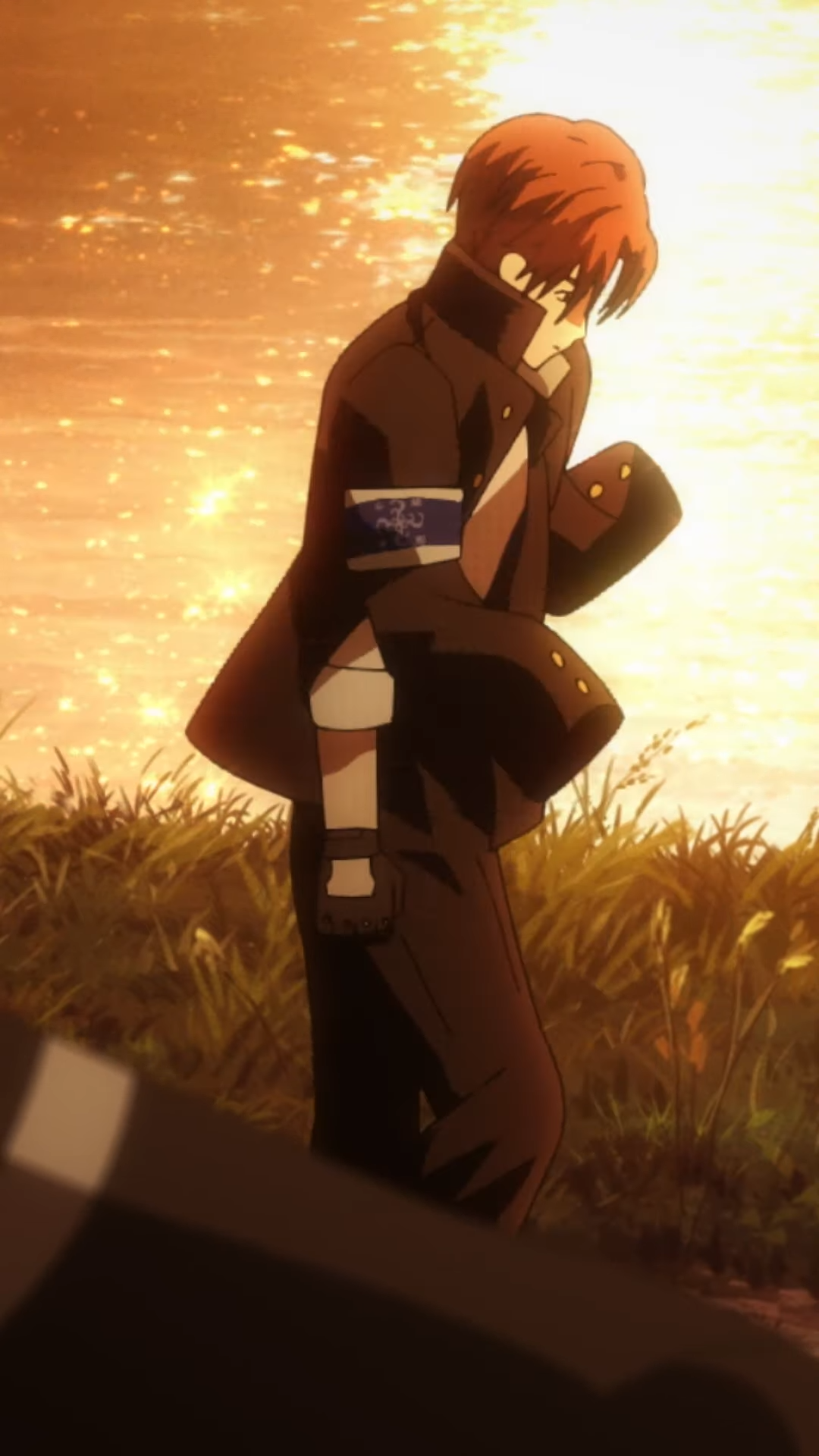 a young man with red hair, wearing a dark uniform with a white armband, walks along a grassy path at sunset. the lighting is warm and backlit, creating a silhouette of his figure against the bright orange sky.