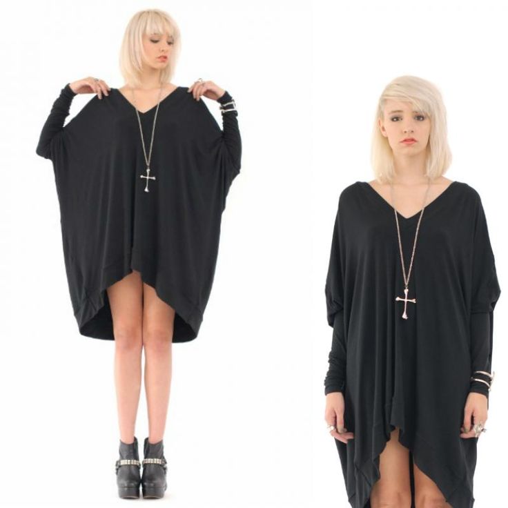 the image shows a woman wearing a black, oversized dress with long sleeves and a vneck. she is wearing a necklace with a cross pendant. the woman has blonde hair and is wearing boots. she also has rings and bracelets on her hands. the background is white.