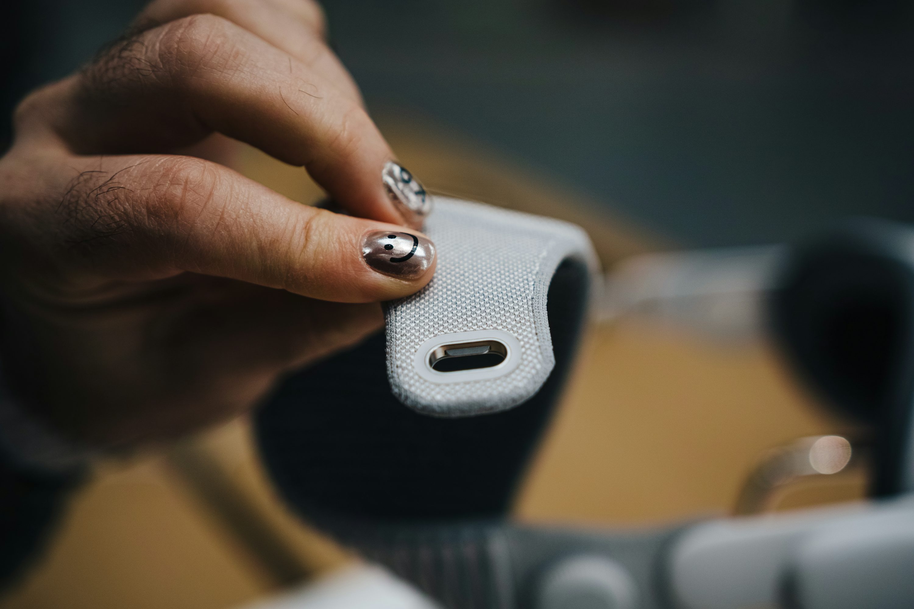 a hand with smiley face nail art is holding a gray fabric headband with metal detailing. the headband is likely for apple airpods max headphones.