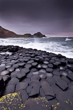 a view of a rocky shoreline on a dark and stormy day. the waves are crashing against the rocks, which are black and grey. the sky is dark and cloudy, and the water is choppy. the scene is dramatic and powerful.