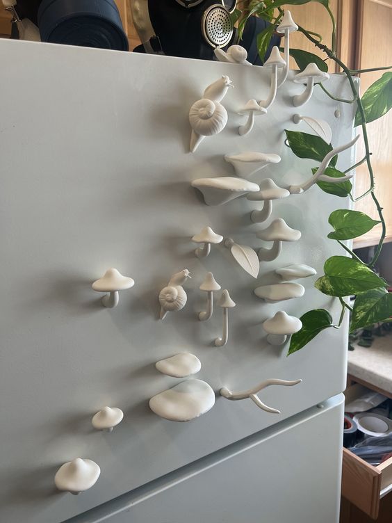 a white refrigerator decorated with a variety of white ceramic mushroom and snail magnets. the magnets are arranged in a whimsical fashion, creating a unique and eyecatching display. the refrigerator is located in a kitchen and is part of a home's interior design.