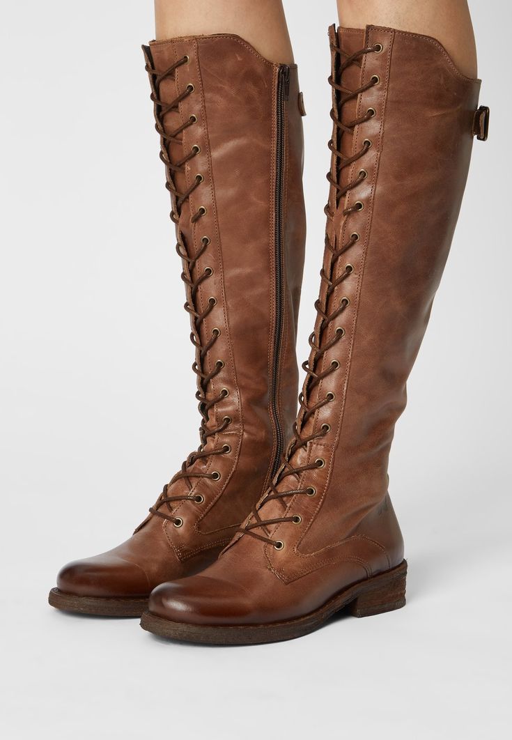 a pair of brown leather kneehigh boots with laceup detailing. the boots have a casual, slightly distressed look. the image is taken from the front and shows the boots being worn by a woman.  the woman's legs are crossed. the boots are a great choice for a casual and stylish look.