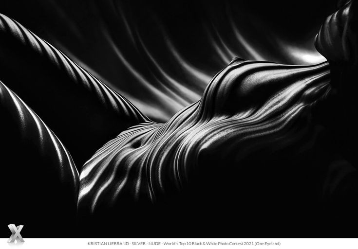 the image is a black and white photograph of a female nude. the subject is positioned lying down, and the body is covered with what seems like a rippled fabric, creating a strong contrast of light and shadow. the lines and curves emphasize the form of the body. the overall effect is abstract and artistic, creating a sensual and elegant mood. the photo is credited to kristian liebrand and was part of the world's top 10 black & white photo contest 2021, organized by one eyeland.