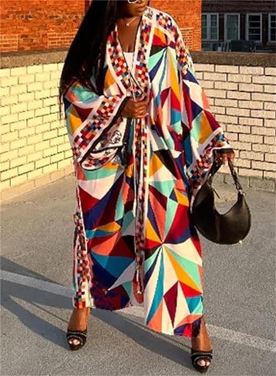 a woman is standing in front of a brick wall, wearing a colorful geometricpatterned kimono, black sandals, and sunglasses. she is holding a black handbag. she is also wearing jewelry.