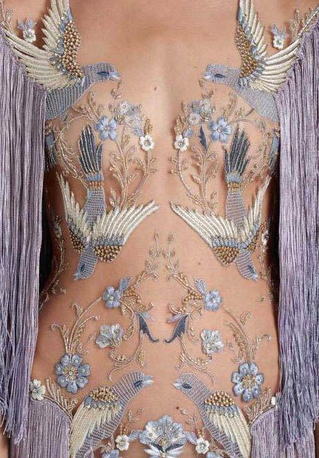 a closeup of a woman's torso adorned with intricate embroidery. the delicate, floral pattern features delicate birds and intricate designs. the dress is a piece of art, with delicate beads and lace accents.