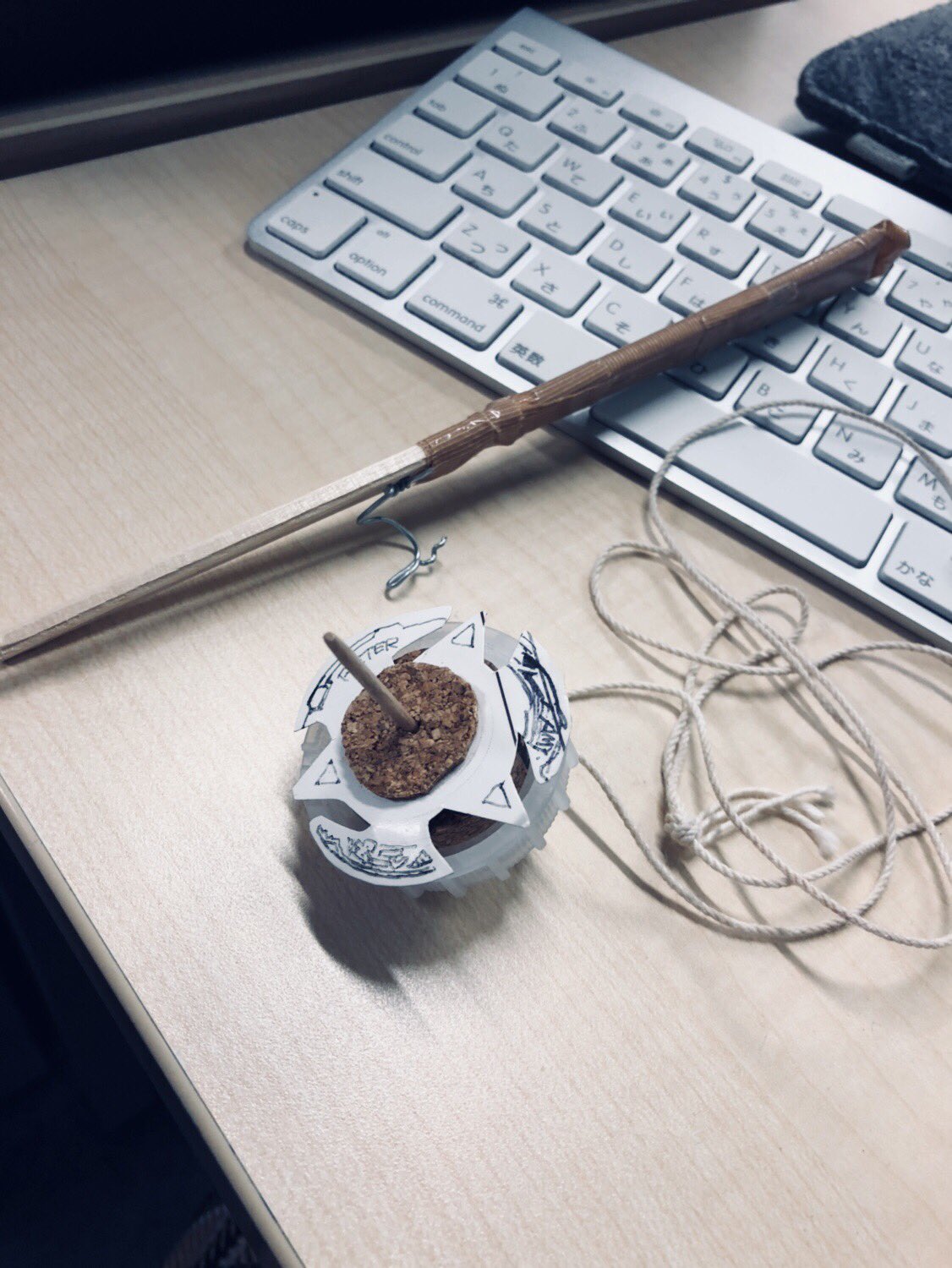 a wooden spinning top with a string, a stick and a keyboard are on a wooden desk.```