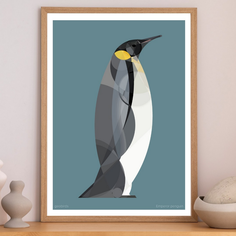 a minimalist geometric illustration of an emperor penguin against a blue background. the penguin is depicted with a yellow beak and chest, and its body is made up of simple shapes and lines. the illustration is framed in a natural wood frame.