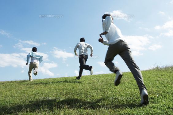 three men are running up a grassy hill under a bright blue sky. the camera is positioned at a low angle, capturing their determined strides as they ascend the slope. the men are spaced apart, suggesting a sense of competition or individual pursuit. the vibrant green of the grass and the clear blue sky evoke a feeling of energy and freedom.