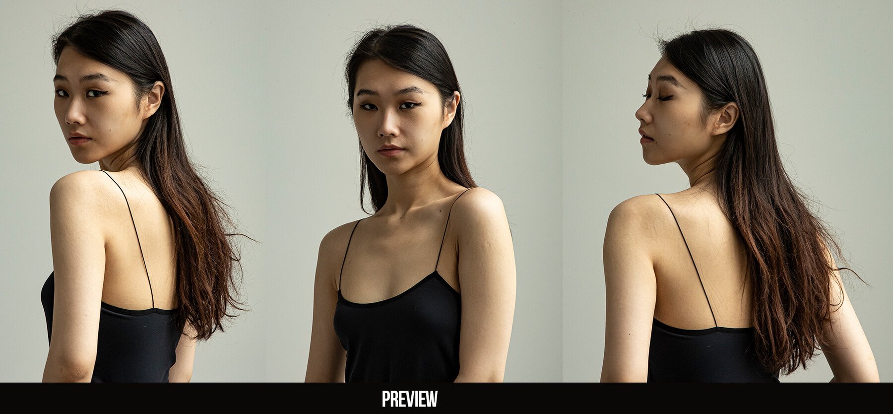 a beautiful asian woman is posing for a portrait. she is wearing a black top with thin straps and her hair is down and flowing. she is standing in front of a white wall in a studio.