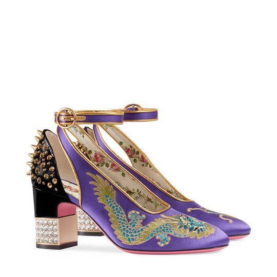 a pair of gucci women's high heels are shown.  the shoes are purple satin with embroidered dragons and floral details. they have a black and gold studded heel and a gold ankle strap.  the shoes are positioned on a white background.