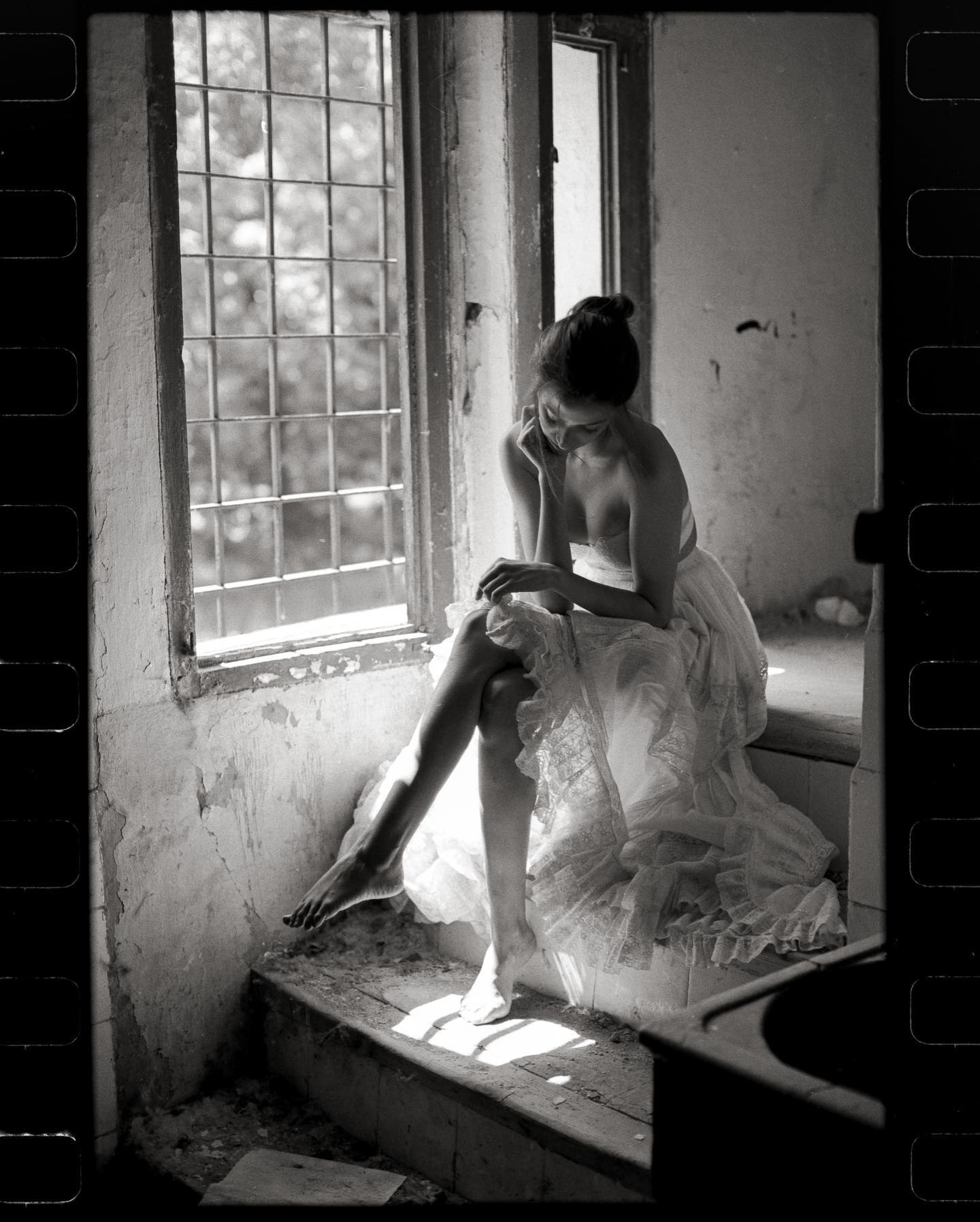 a woman sits on a step in an old, crumbling building. she is wearing a long, white lace dress and her hair is down. she is looking down thoughtfully. the window behind her is open, and the sun is shining through. the light creates a dramatic shadow on the wall. the scene is very beautiful and peaceful, with a touch of melancholy.