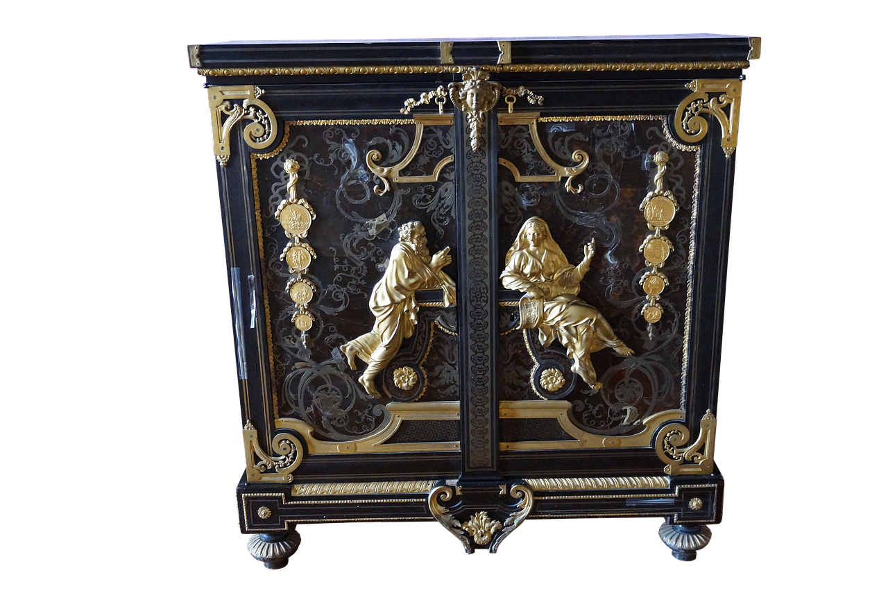 the image shows a detailed antique chest of drawers. the chest has a black background with ornate gold relief and statues. the carvings depict figures and ornamental designs. the piece has a black and gold color scheme with a marble or light colored top. the entire piece is set against a plain black backdrop.