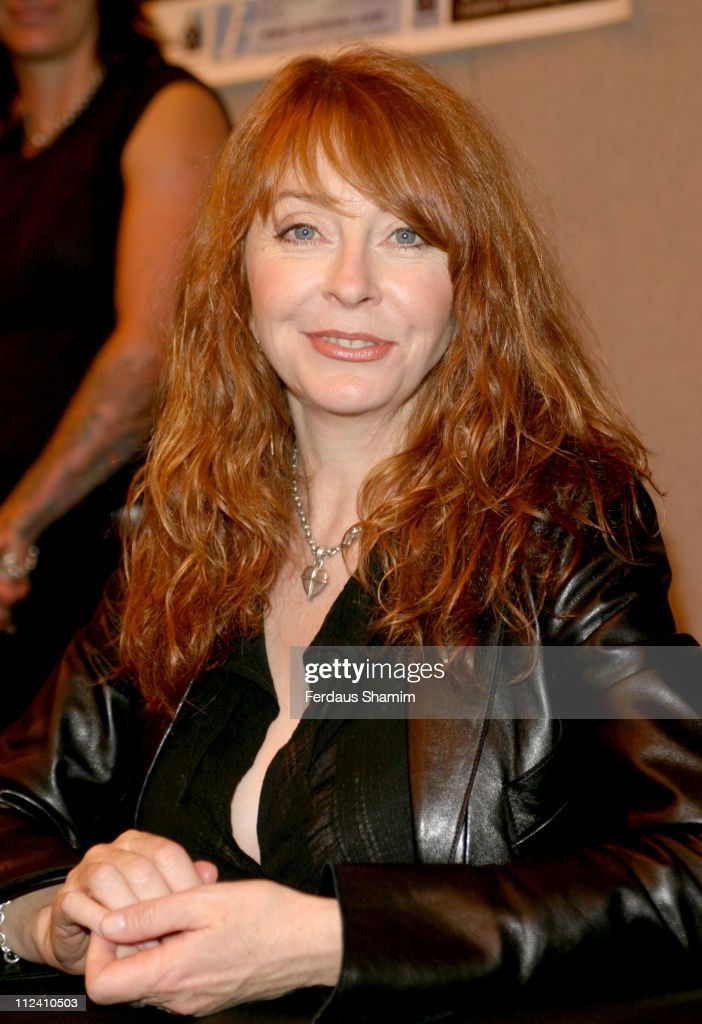 a woman with long red hair is wearing a black leather jacket and looking intently at the camera. she is sitting in a studio setting and appears to be a model or actress.