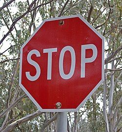 a red and white octagonal stop sign is mounted on a pole, with trees and branches visible in the background. the sign clearly displays the word "stop" in large, white letters. the scene appears to be outdoors during the daytime.