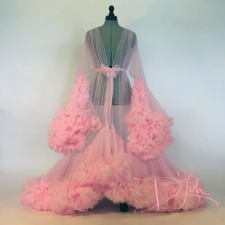 a pink tulle robe with voluminous ruffles on the sleeves and hem is displayed on a mannequin against a plain background. the robe is sheer and tied at the waist with a delicate bow.