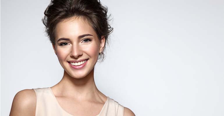 Brunette with pulled up hair and beige silk top smiling at you