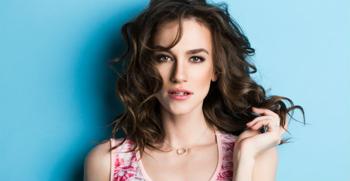 Close up of sassy-looking brunette in floral tank top against light blue backdrop