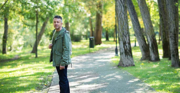 Active middle-aged man with backpack on walking path in park