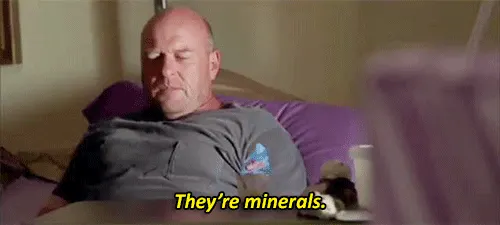 Hank Schrader from Breaking Bad reclines in bed with a stern look, saying “They’re minerals” in yellow subtitle text.