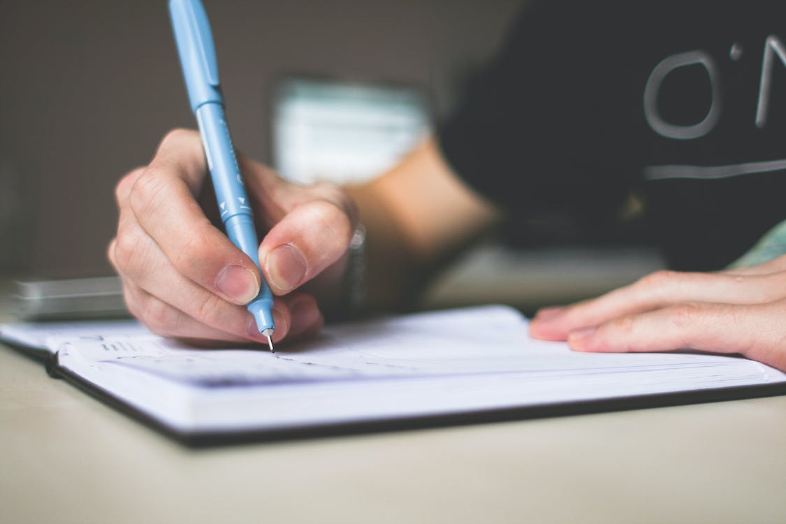 Free Person Holding Blue Ballpoint Pen Writing in Notebook Stock Photo