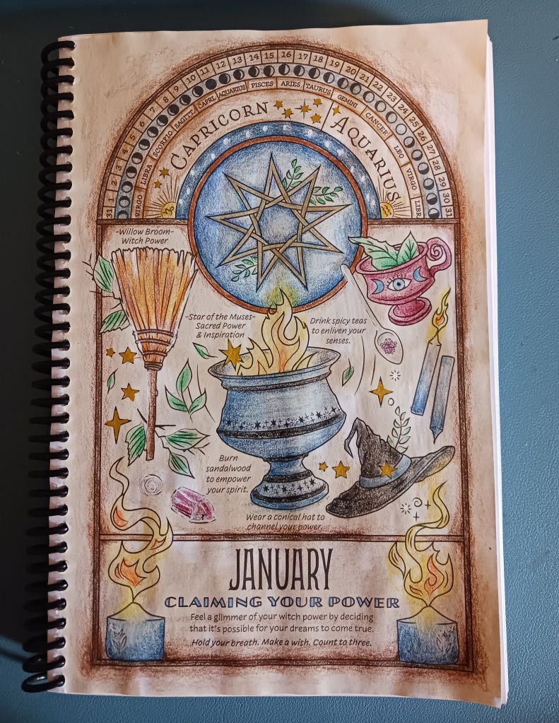 Image of a spiral-bound planner open to a coloring page for the month of January. There are many magical-themed objects such as a witch's hat and broom, candles, a crystal, a cauldron, and a 9-pointed start as a central focal-point. The page has been colored using the mediums of coffee staining, colored pencil, and a gel pen with blue, black, yellow, orange, mulberry, and rich browns being the dominant colors.