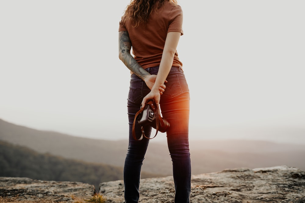 mulher na camisa marrom de manga comprida e jeans jeans azuis segurando bolsa de couro marrom