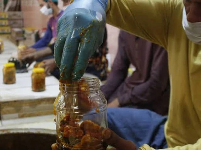 A woman preparing traditional mango pickle in a clay jar, a scene becoming rarer in South Punjab.
