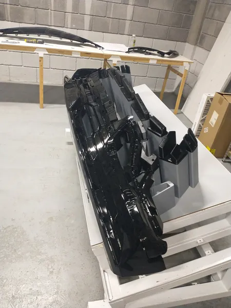 Jig de ensamble gris impreso en 3D sosteniendo una fascia automotriz negra en el taller