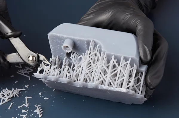Manos con guantes cortando con pinzas los soportes de una pieza impresa en resina
