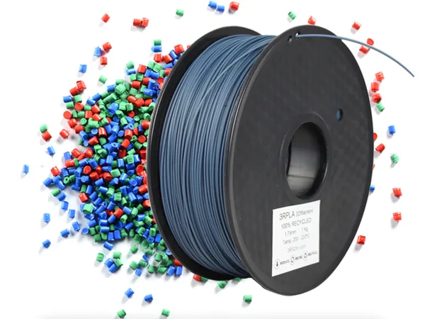 Carrete de filamento de PLA reciclado rodeado de pellets de plástico de colores