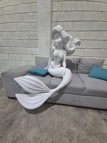 Sirenita impresa en 3D en blanco antes de pintar, sentada en un sillón para dimensionar su escala real