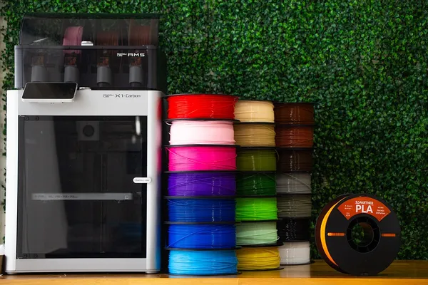 Impresora 3D con sistema multimaterial junto a columnas de carretes de filamento PLA de colores