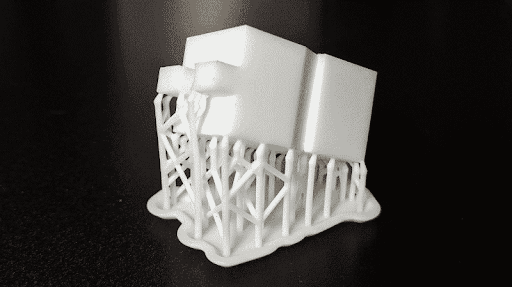 Pieza blanca impresa en 3D sostenida por soportes delgados sobre una base