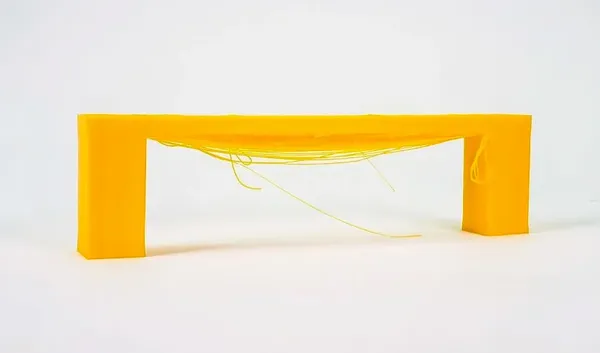 Puente amarillo impreso en 3D con hilos colgando por un tramo demasiado largo sin soporte
