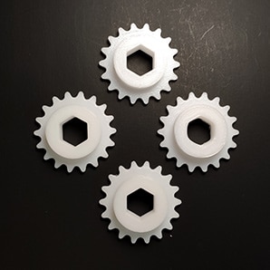 Cuatro engranes blancos con barreno hexagonal impresos en 3D como ejemplo de pieza funcional