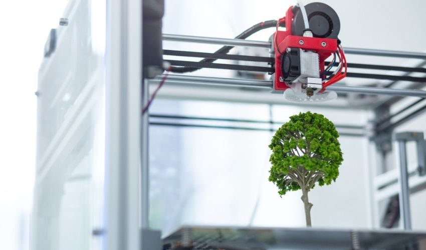 Impresora 3D con un árbol impreso en la cama, que representa el lado sustentable de la manufactura aditiva