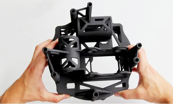 Manos sosteniendo una estructura negra impresa en 3D, compleja y rígida, típica de piezas de nylon