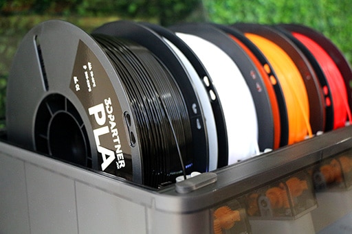 Carretes de filamento PLA 3DPartner en negro, blanco, naranja y rojo montados en un sistema multimaterial